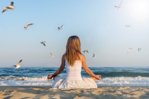 Woman meditating at the sea with flying seagulls